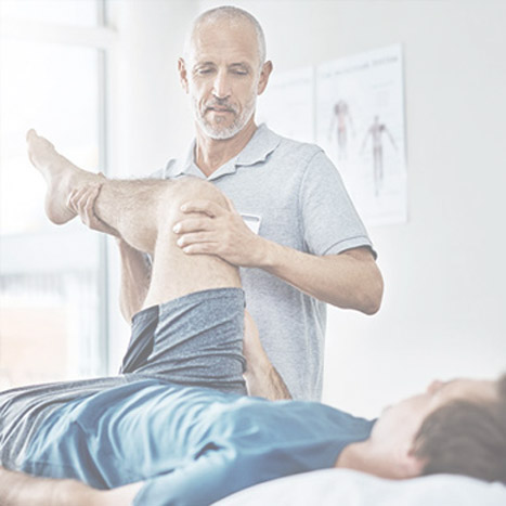 Ein Mann wird von einem Physiotherapeuten am Bein behandelt.