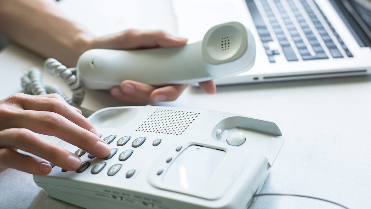 Eine Frau wählt eine Telefonnummer auf einem Festnetztelefon. In der anderen Hand hält sie den Telefonhörer. Nahaufnahme der wählenden Hand. Eine Frau wählt eine Telefonnummer auf einem Festnetztelefon. In der anderen Hand hält sie den Telefonhörer. Nahaufnahme der wählenden Hand.