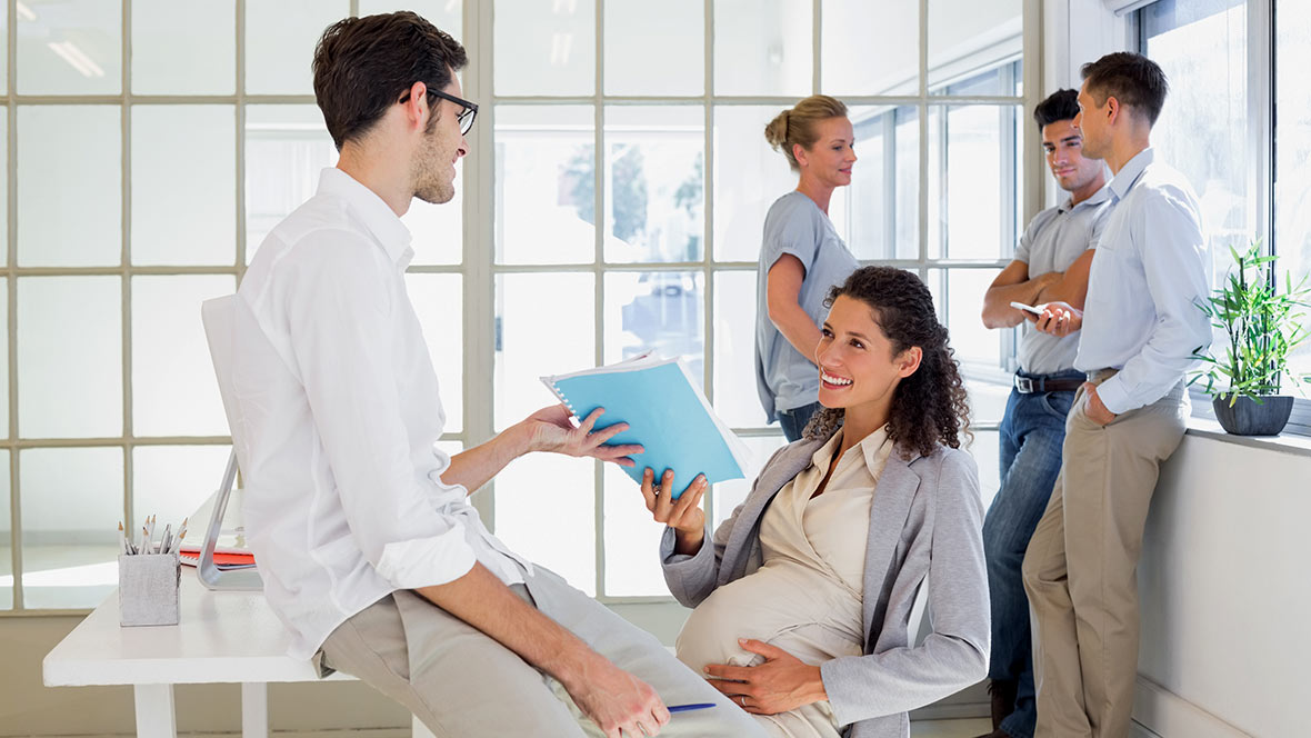 Schwangere Frau am Arbeitsplatz im Gespräch mit Kollegen Schwangere Frau am Arbeitsplatz im Gespräch mit Kollegen