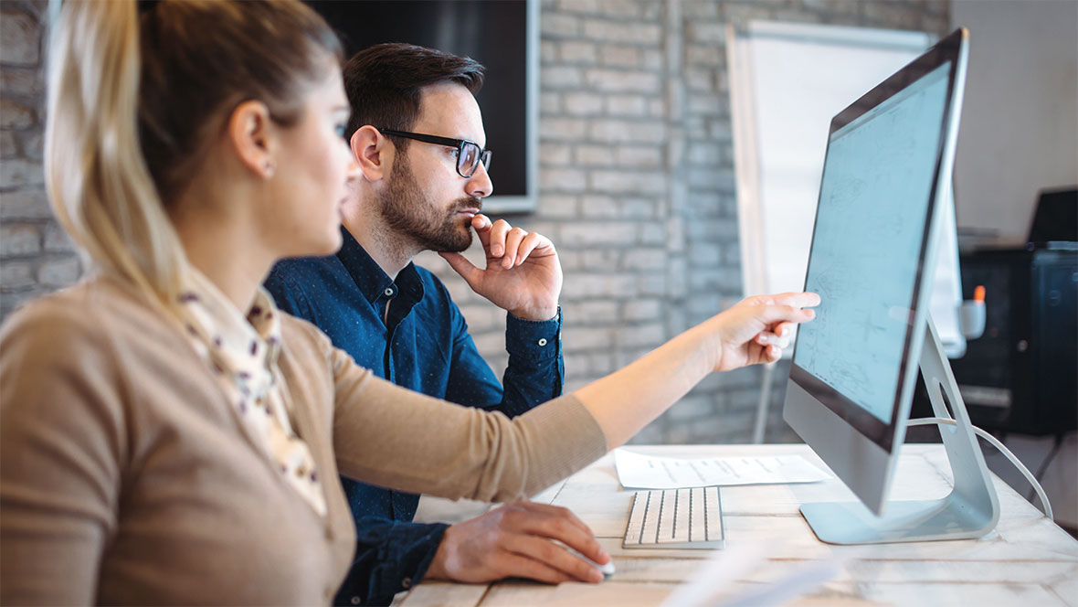 Eine Frau und ein Mann am Arbeitsplatz vor einem Monitor. Die Frau zeigt auf eine Stelle am Monitor. Eine Frau und ein Mann am Arbeitsplatz vor einem Monitor. Die Frau zeigt auf eine Stelle am Monitor.