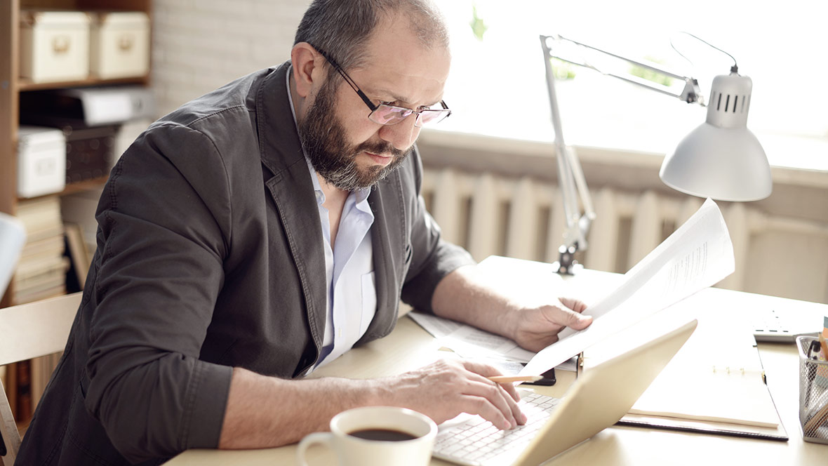 Ein Mann sitzt am Schreibtisch und arbeitet mit einem Laptop.