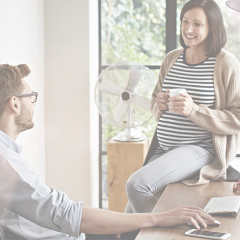 Ein Mann sitzt an einem Schreibtisch im Büro, eine schwangere Frau sitzt neben ihm, auf der Ecke des Schreibtisches. Ein Mann sitzt an einem Schreibtisch im Büro, eine schwangere Frau sitzt neben ihm, auf der Ecke des Schreibtisches.