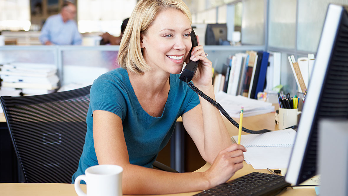Eine Frau telefoniert am Schreibtisch in einem Büro. Eine Frau telefoniert am Schreibtisch in einem Büro.
