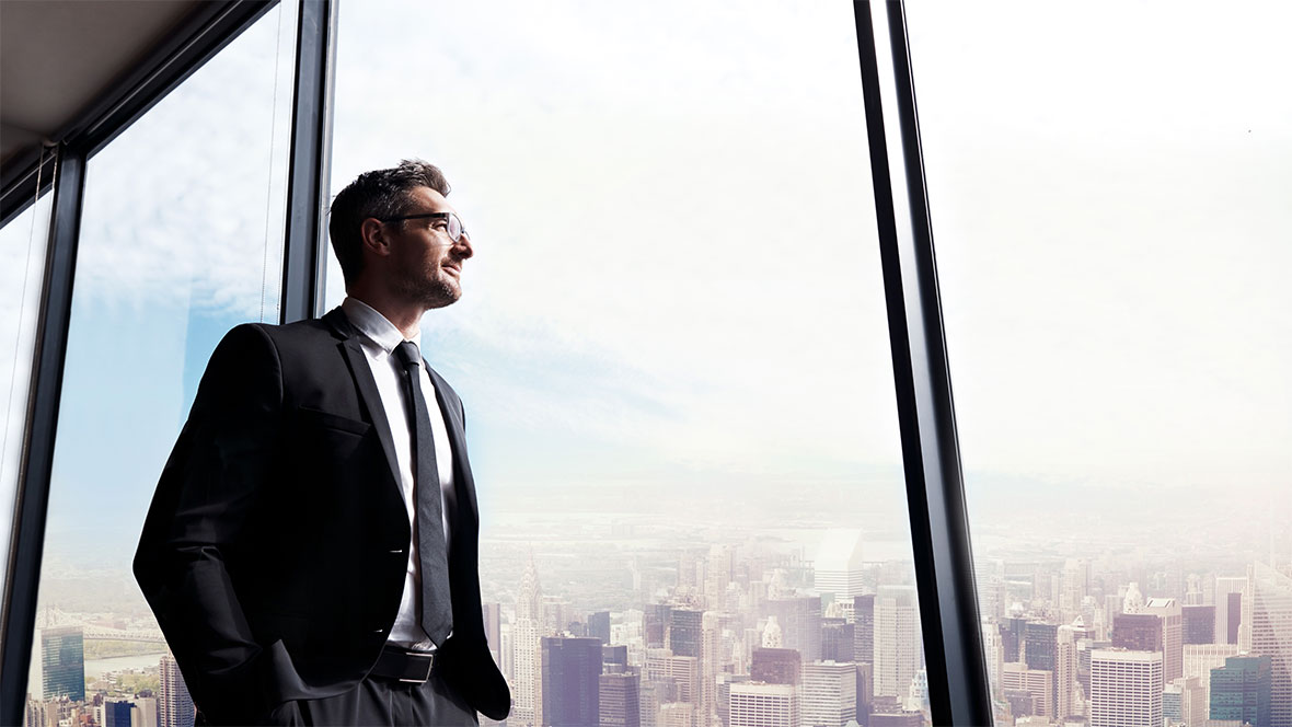 Geschäftsmann schaut aus dem Fenster eines Hochhauses in die Ferne Geschäftsmann schaut aus dem Fenster eines Hochhauses in die Ferne