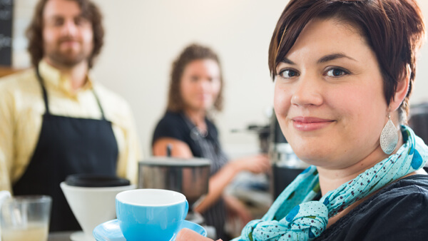 Eine Frau steht in einem Cafe und hält eine blaue Tasse hoch.